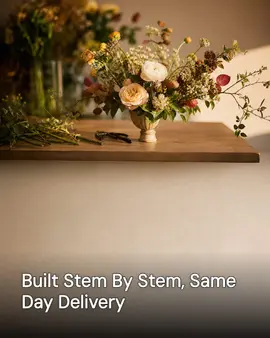 Generated post: a finished autumn-toned floral arrangement in a low urn vase on a florist's workbench with loose stems and clippers scattered nearby, headline about building arrangements stem by stem with same-day delivery baked into the image